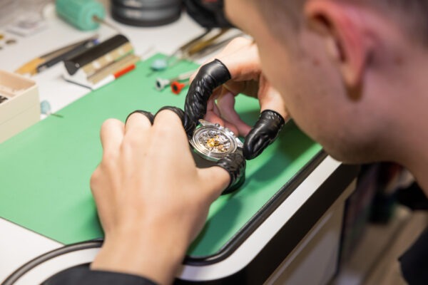 Uhrmacher prüft ein Uhrwerk mit Handschuhen an der Werkbank